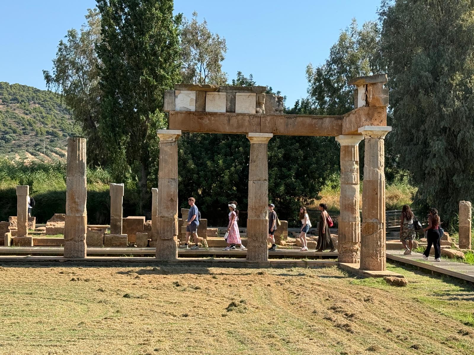 A line of students walking behind the columns that remain of an ancient Greek sanctuary.