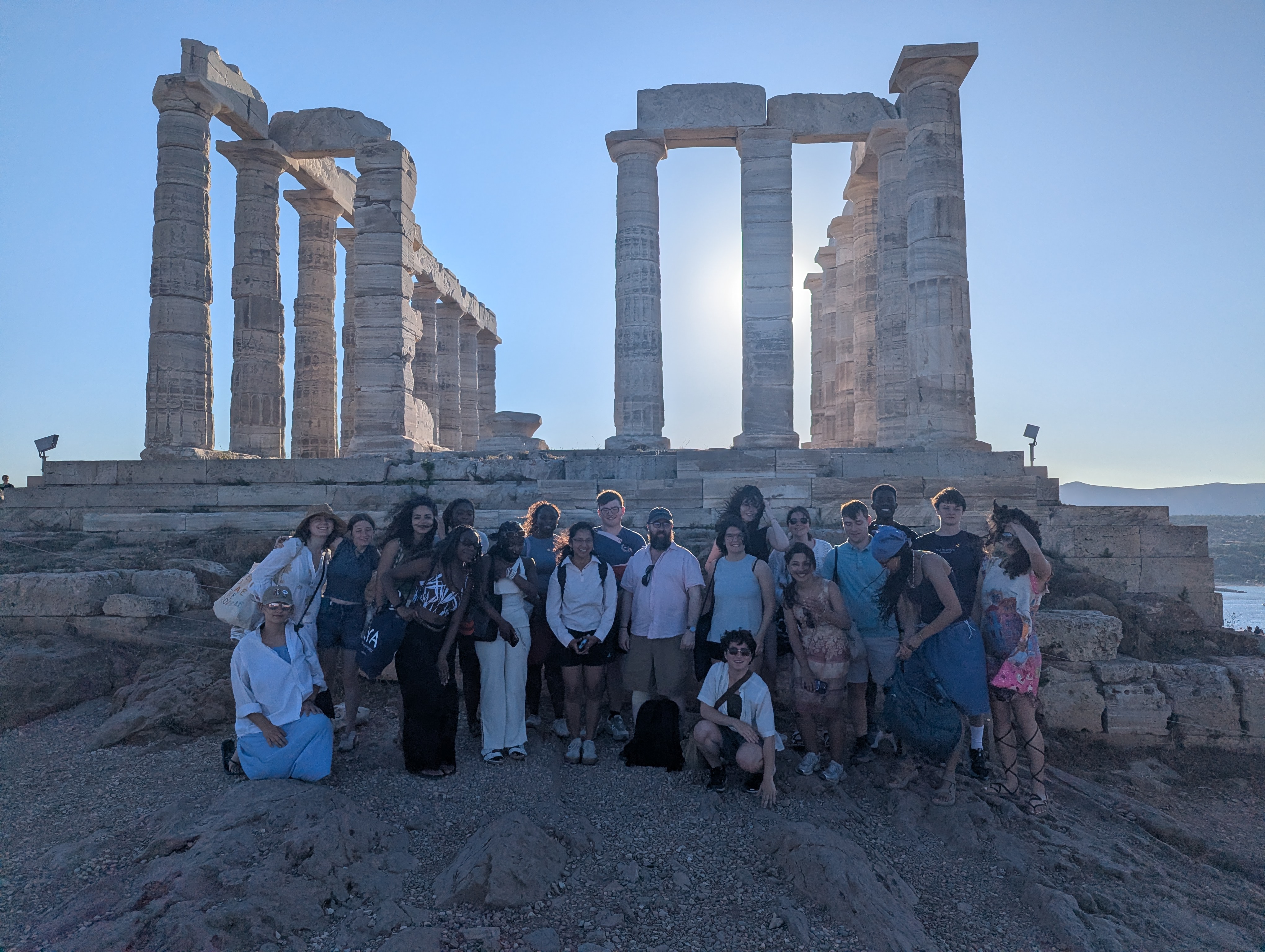 Students and Prof. Platte gathered together in front of the remains of a large Greek temple that is backlit by the sun.