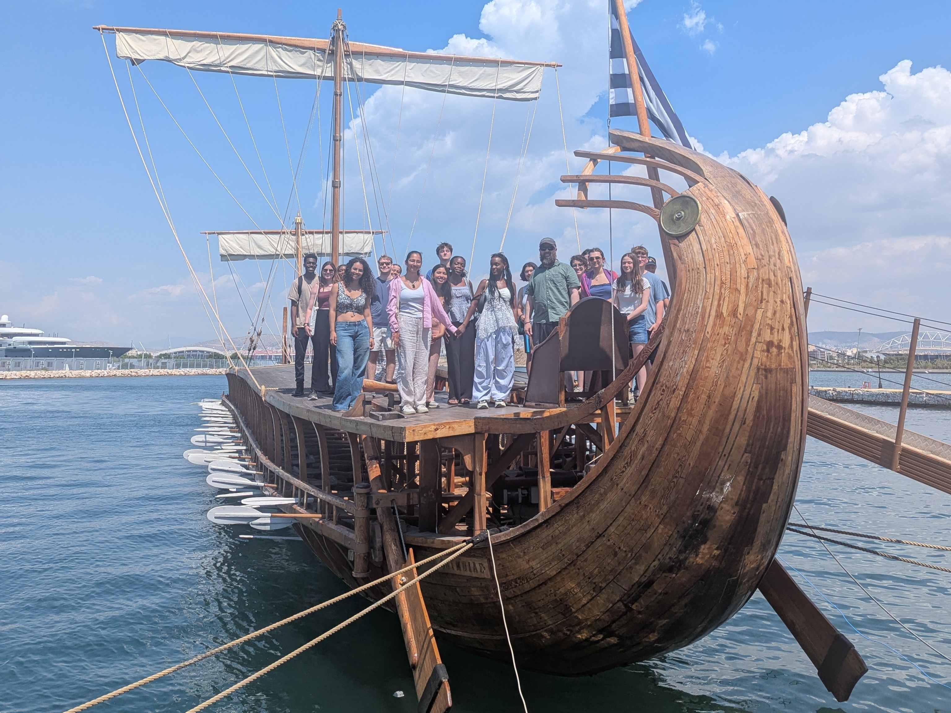 Students and Prof. Platte standing in a crowd on an ancient trireme replica floating in the water.